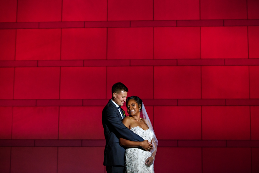 A bride and Groom hold each other in front of a colorful wall after their wedding at The National Constitution Center.